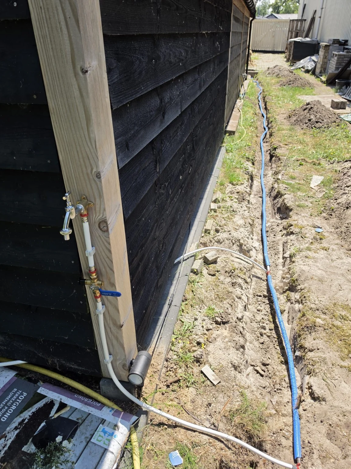 Nieuw aangelegde buitenleiding en buitenkraan bij een bijgebouw